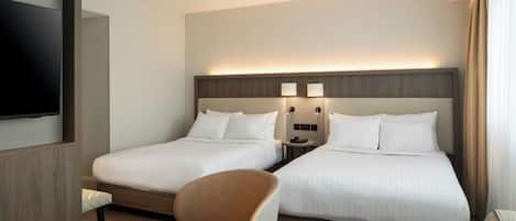 Habitación de hotel con dos camas, televisión, una silla y una mesita de noche con lámparas.