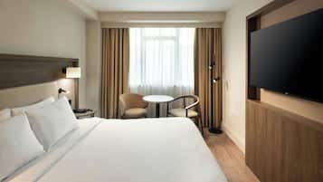 A hotel room with a large bed, a TV, a desk with two chairs, and a window with curtains.