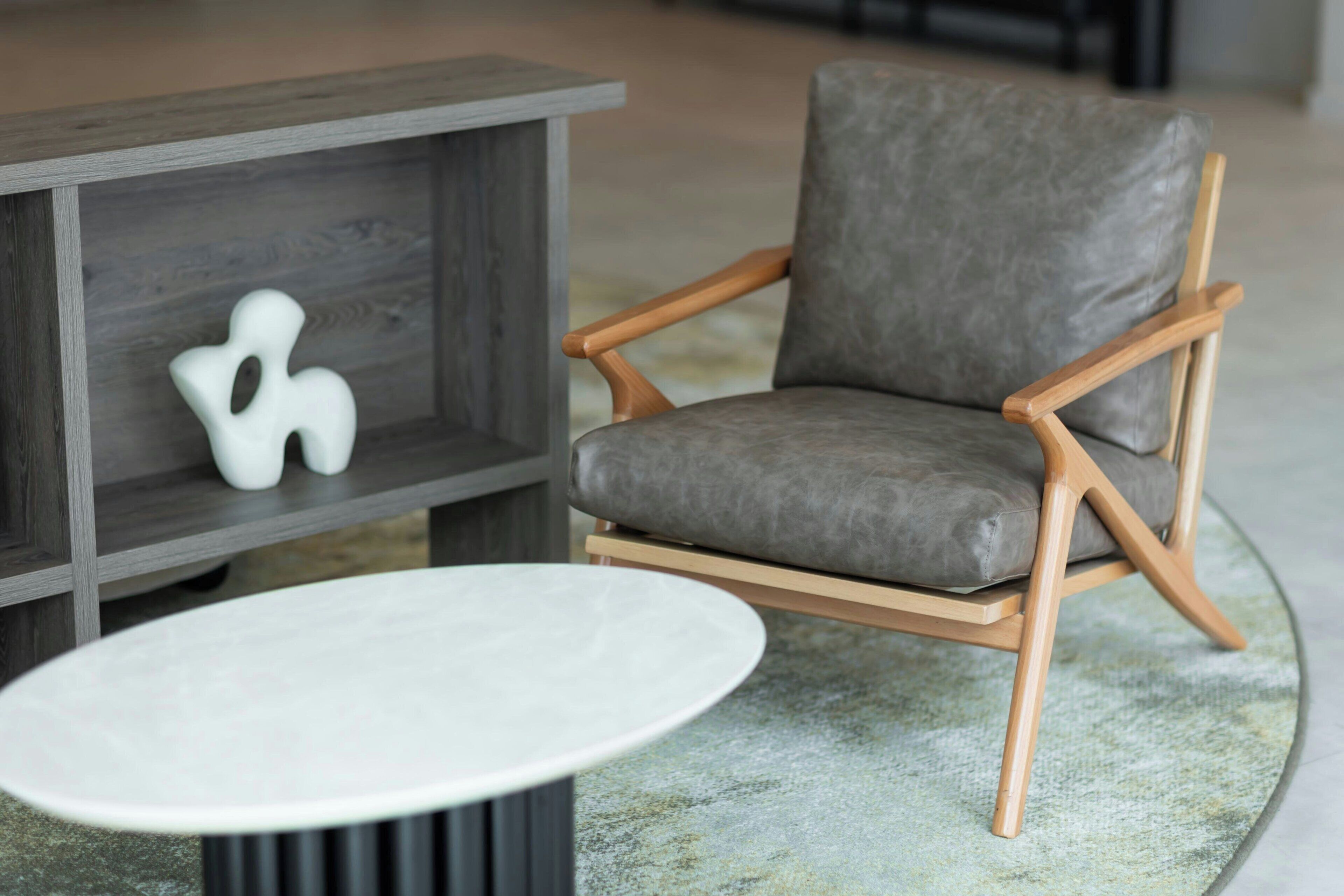 Une pièce moderne avec un fauteuil à revêtement gris, une table d’appoint en bois et une table ronde blanche.