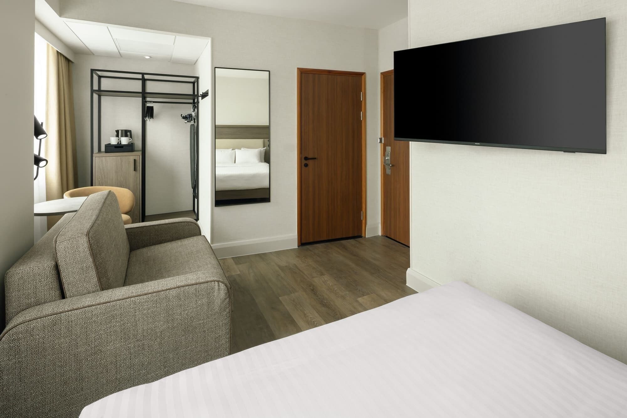 Ein Hotelzimmer mit Bett, Fernseher, Sofa, Spiegel, Kleiderschrank und einem Badezimmer mit Dusche und Toilette.