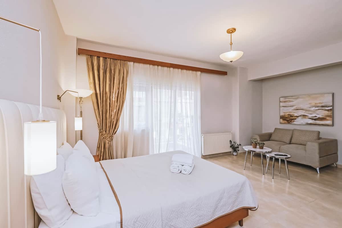 A hotel room with a bed, a sofa, a small table with a lamp, and a painting on the wall.