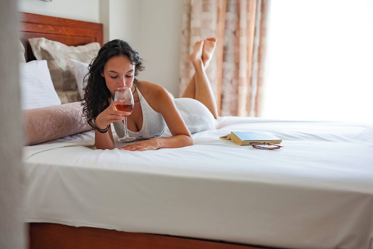A person lying on a bed with a book and a glass of drink.