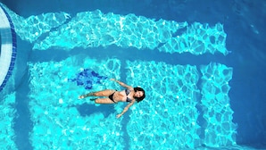 Una persona flotando en una piscina azul cristalina con juegos de luz en el agua.