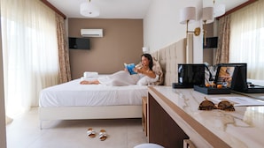 Habitación de hotel con cama, mesita de noche con lámpara, televisor y ventana con cortinas.