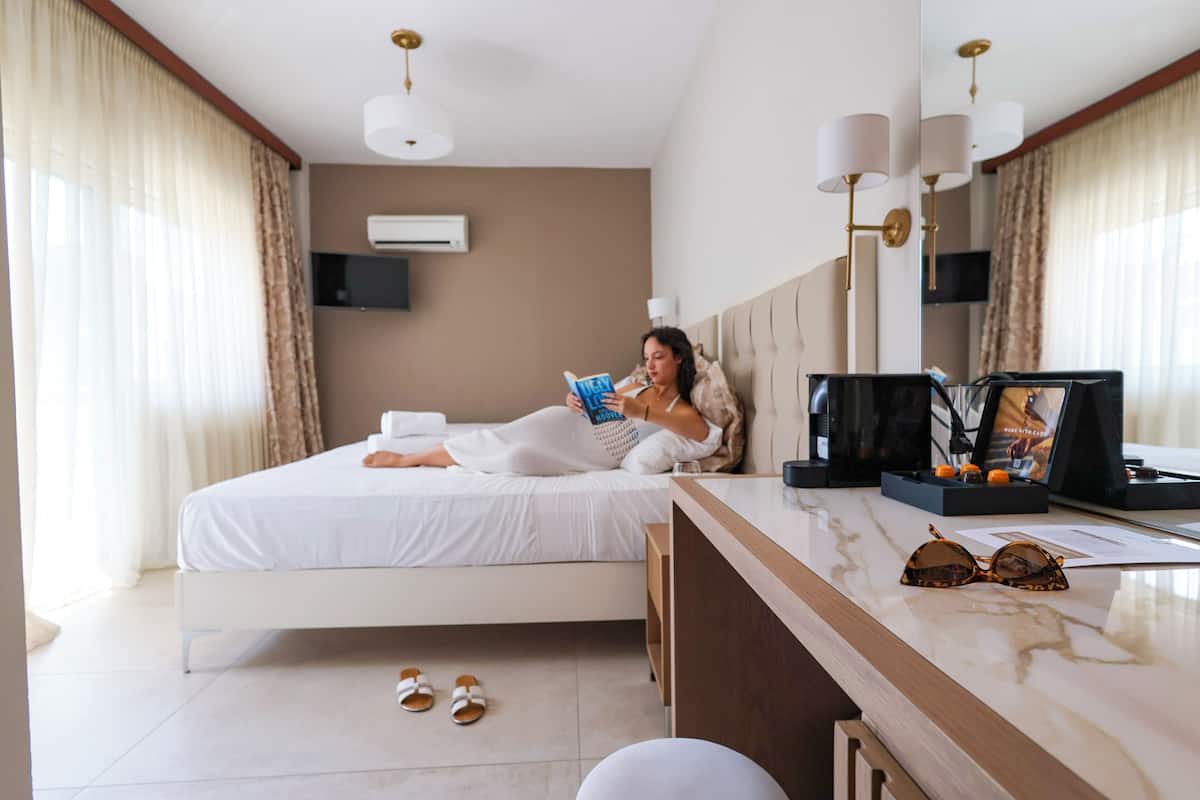 A hotel room with a bed, a bedside table with a lamp, a TV, and a window with curtains.