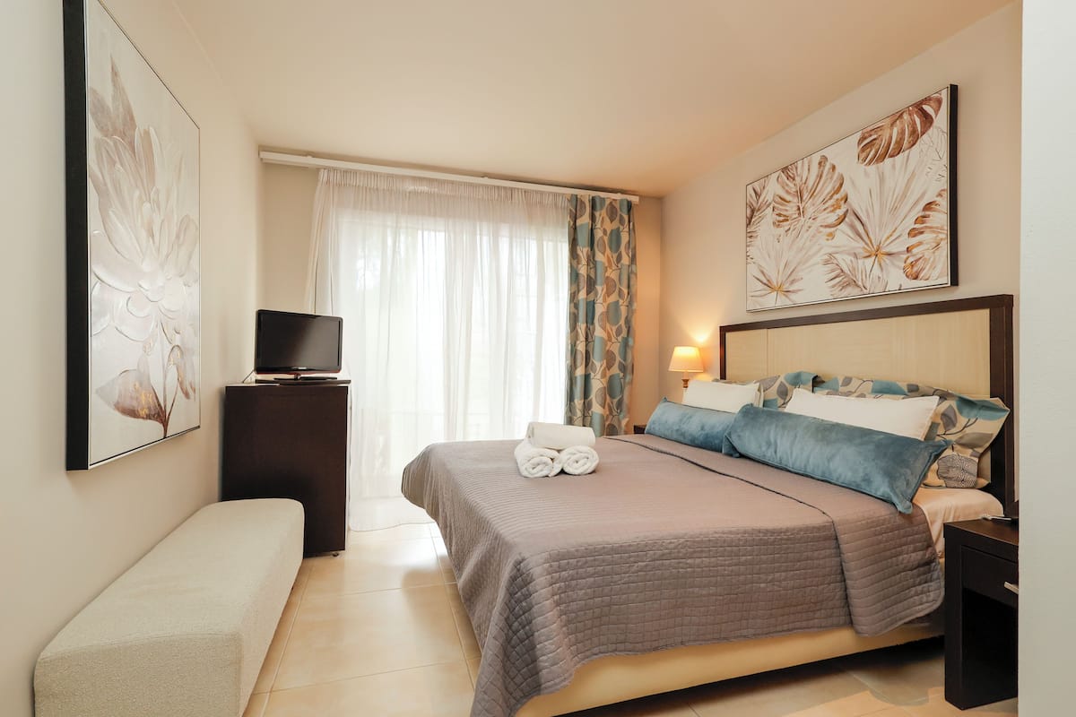 A neatly arranged bedroom with a bed, bedside table, TV, and artwork on the walls.