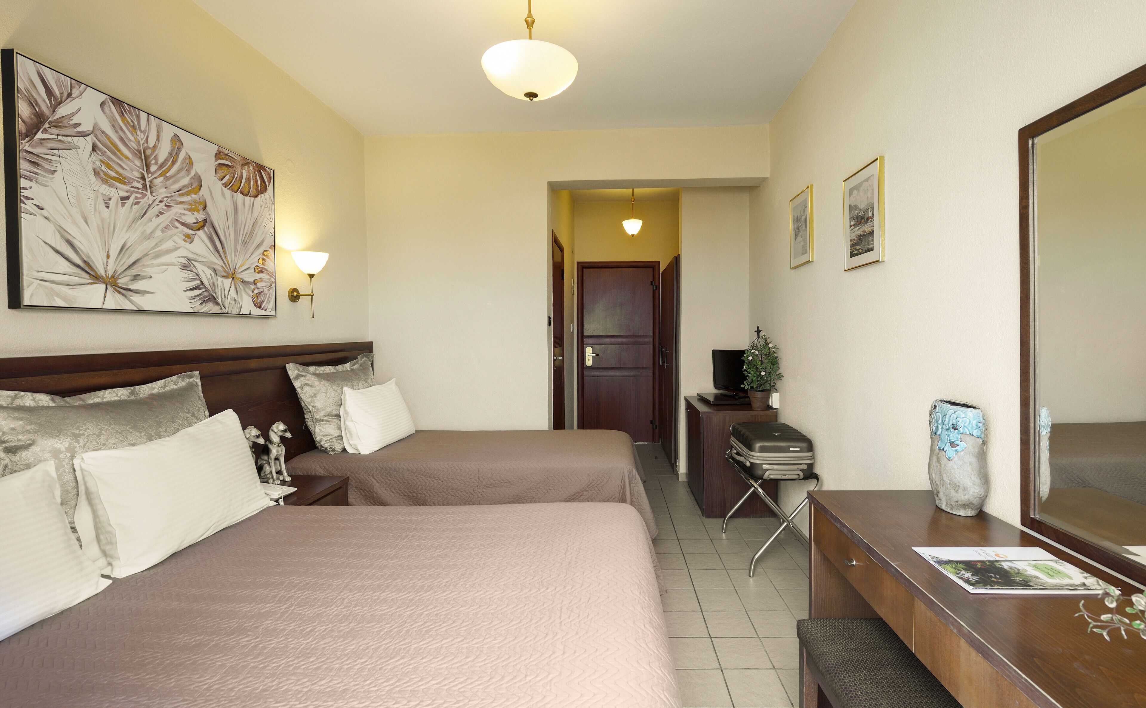 A hotel room with two beds, a desk with a computer, a TV, and a large mirror.