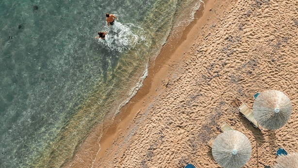 Vista aérea de una playa con agua cristalina, una orilla arenosa y varias sombrillas de playa.