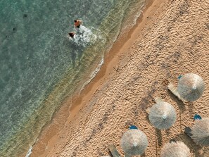 An aerial view of a beach with clear water, a sandy shore, and several beach umbrellas. - Alkyonis Hotel (Nea Propontida)