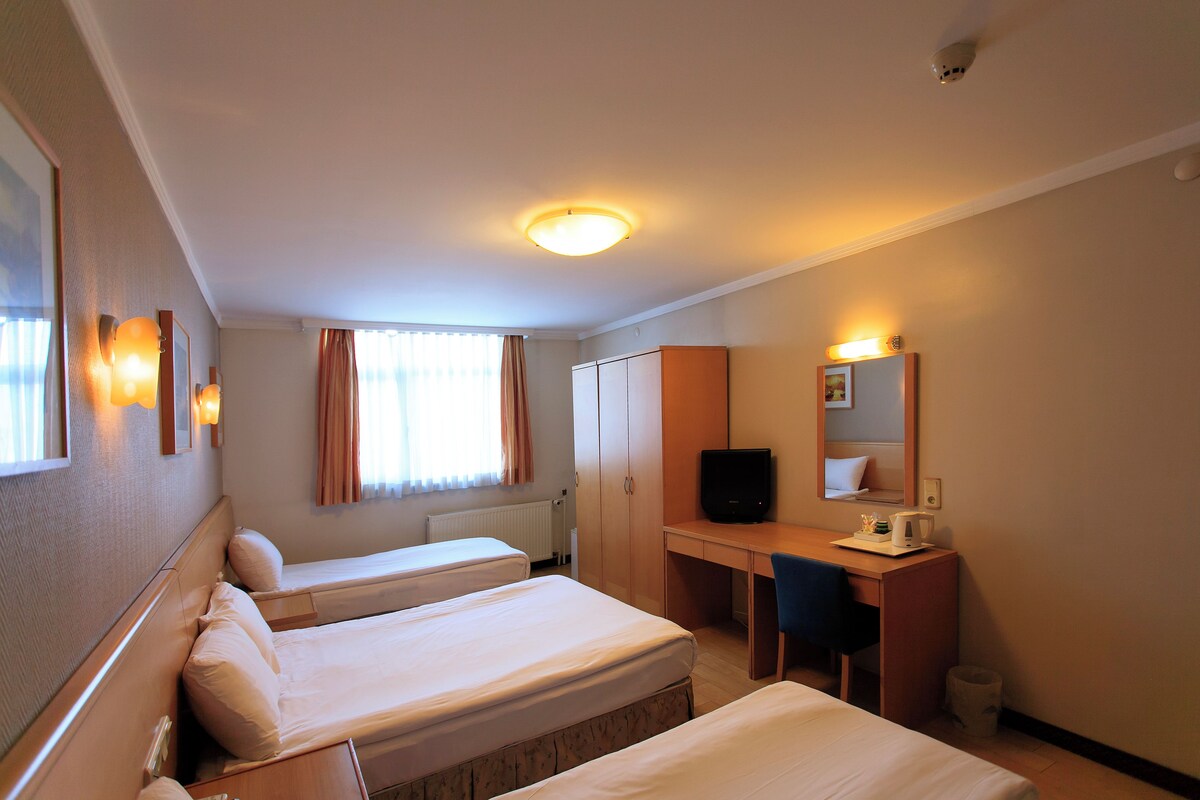 A hotel room with two beds, a desk, a chair, a television, and a window with curtains.