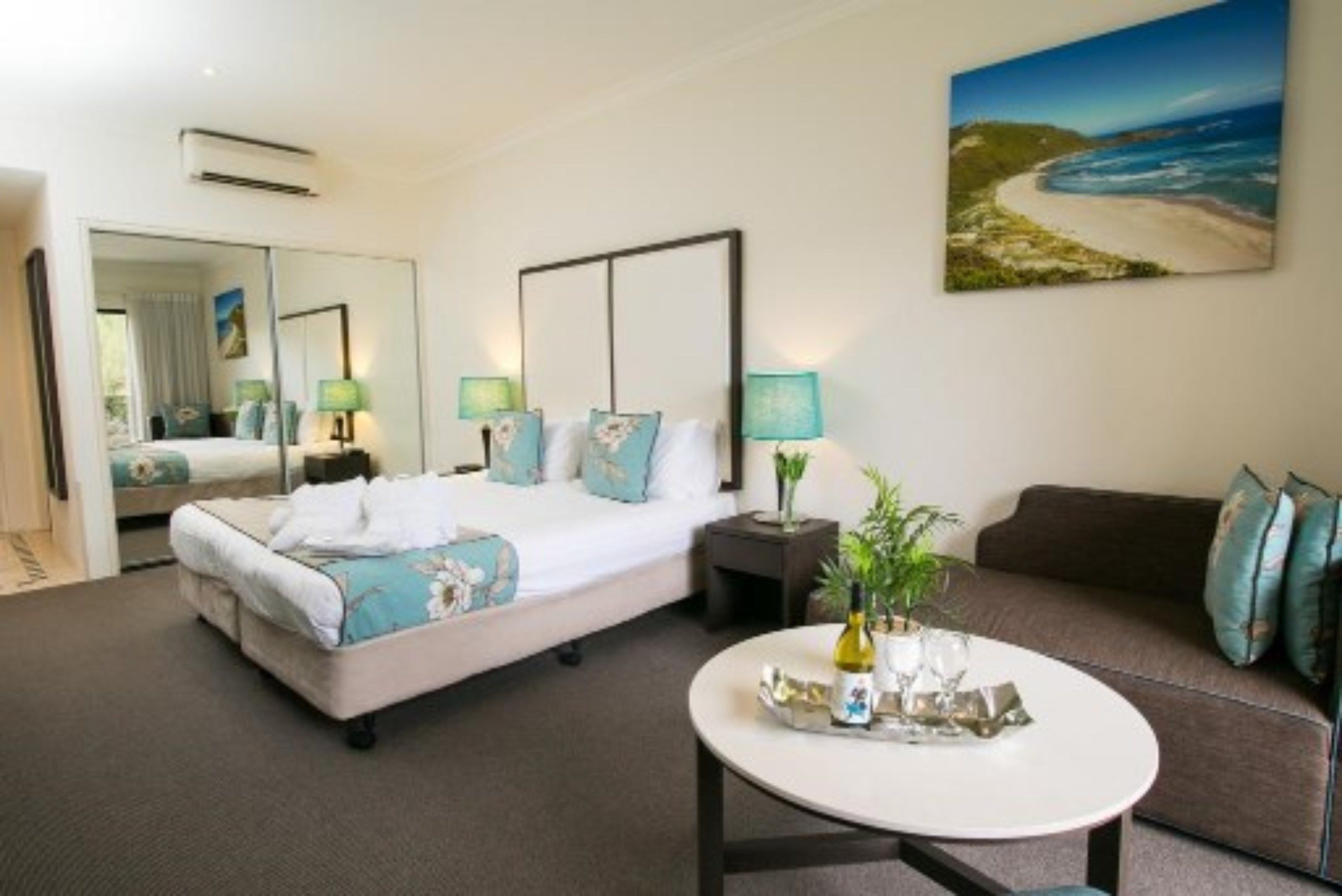 A hotel room with a bed, a sofa, a coffee table, and a painting of a beach.