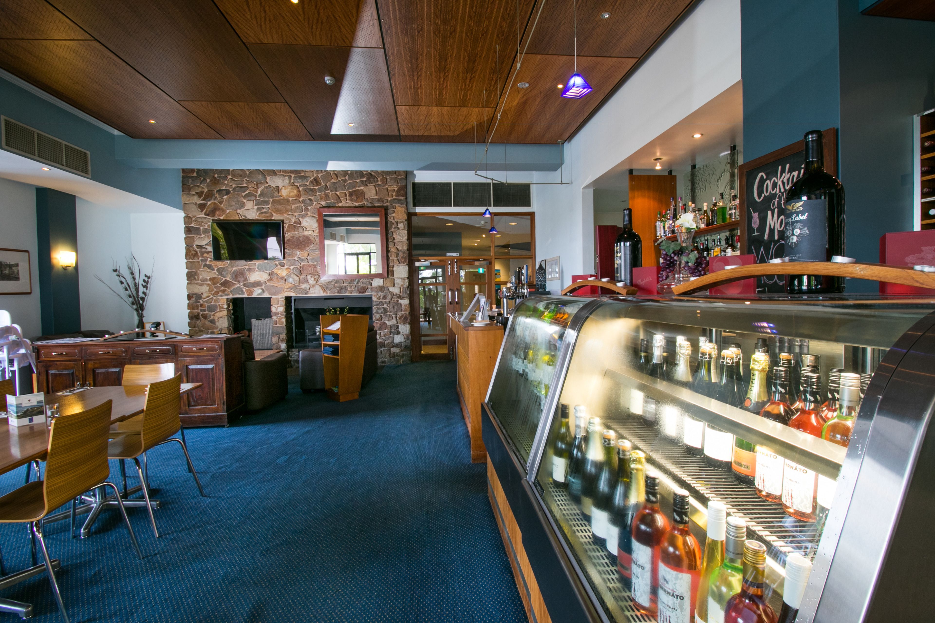 A bar area with a stone wall, wooden ceiling, and a display case of bottles.