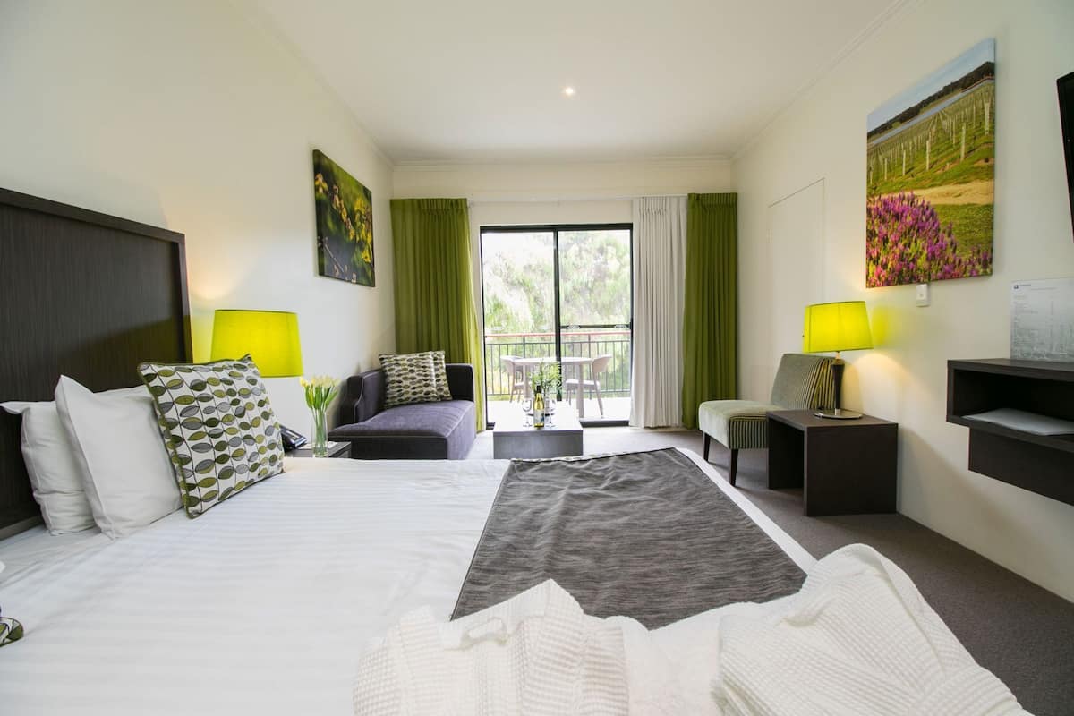 Habitación de hotel con cama, sofá, escritorio, silla, televisión y balcón con mesa y sillas.