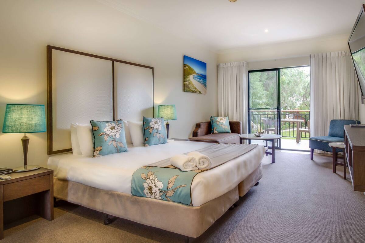 Habitación de hotel con una cama grande, un escritorio, una silla y un balcón con vistas al exterior.