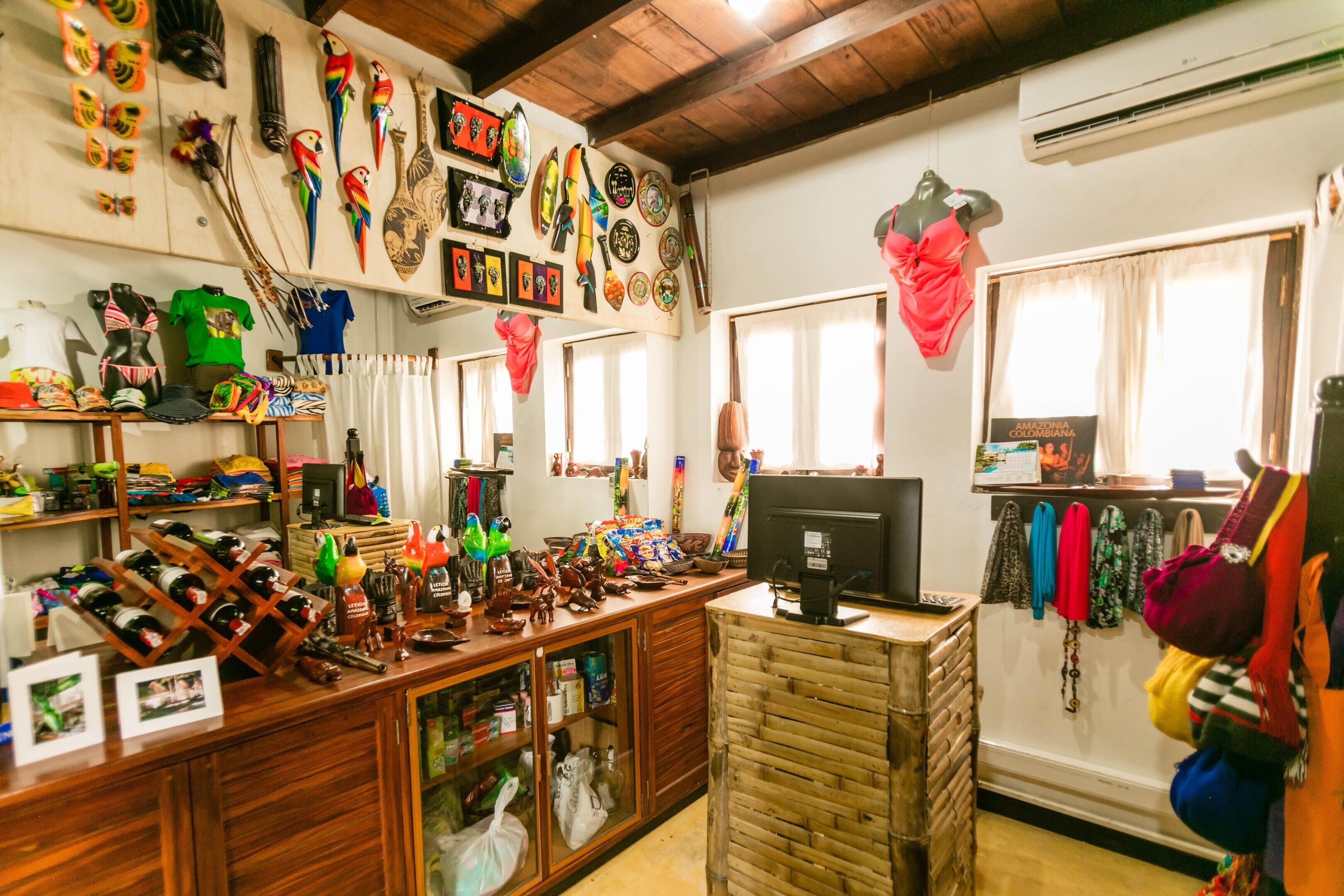 Una habitación con un escritorio de madera, estanterías con diversos objetos, un ordenador y una ventana con cortinas.