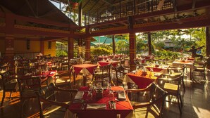 A restaurant with multiple tables and chairs, covered with red tablecloths, and a view of the outdoors. - Decameron Decalodge Ticuna (Leticia)