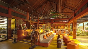 A spacious lobby with a high ceiling, a central seating area with cushions, and a bar area with a sign reading "CAJA". - Decameron Decalodge Ticuna (Leticia)
