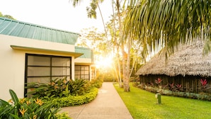 A pathway leading to a building with a green roof and a thatched structure. - Decameron Decalodge Ticuna (Leticia)