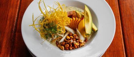 A white plate with a variety of food items including avocado, nuts, and a creamy sauce, placed on a wooden table.