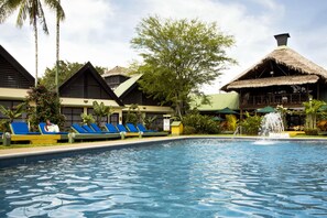 A pool area with lounge chairs and a thatched-roof building. - Decameron Decalodge Ticuna (Leticia)