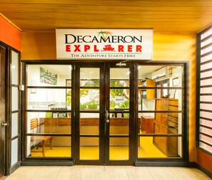 Fachada con un letrero que dice "Decameron Explorer" y un interior de madera visible a través de las puertas de vidrio.