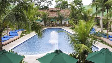 A swimming pool with a water fountain, surrounded by palm trees and lounge chairs.