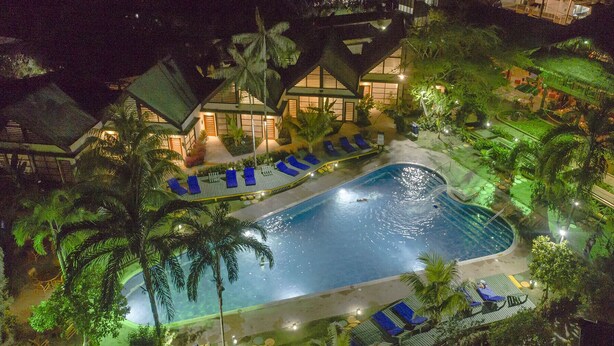 A swimming pool surrounded by lounge chairs and palm trees, with a building in the background. - Decameron Decalodge Ticuna (Leticia)