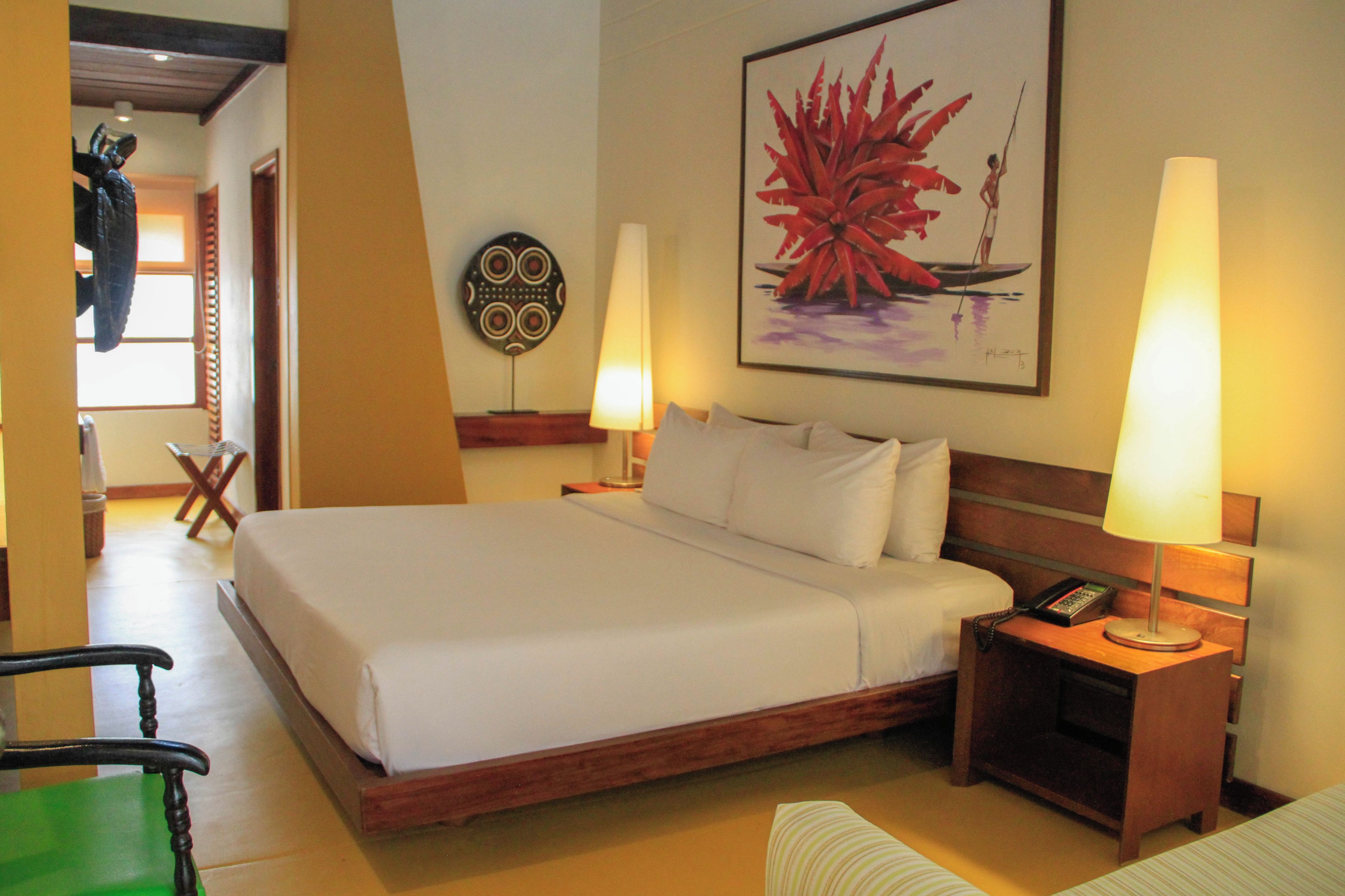 A hotel room with a large bed, two bedside lamps, a nightstand with a phone, a chair, and a wall painting.