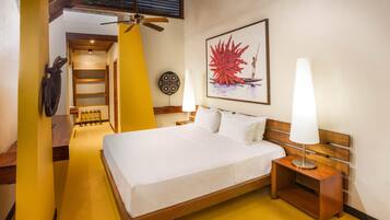 Habitación de hotel con una cama, dos lámparas de noche, un ventilador de techo, un cuadro colgado en la pared y un banco de madera.