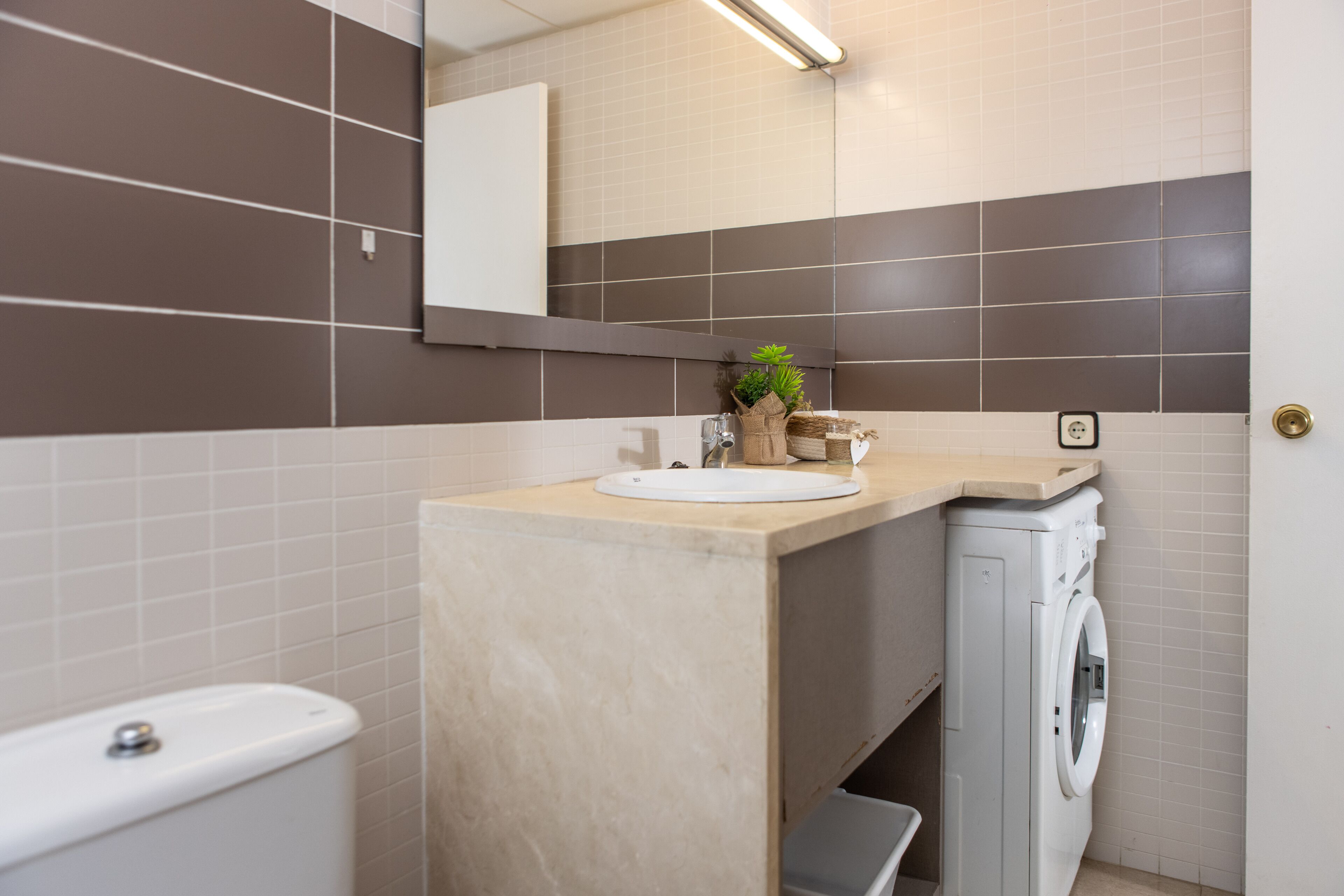 A bathroom with a toilet, sink, mirror, and washing machine.