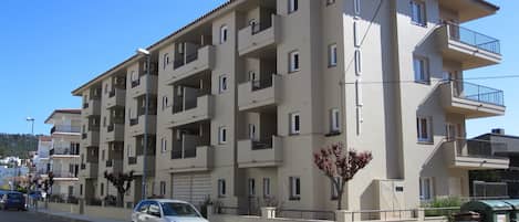 A multi-story residential building with balconies, a crosswalk, and a parked car.
