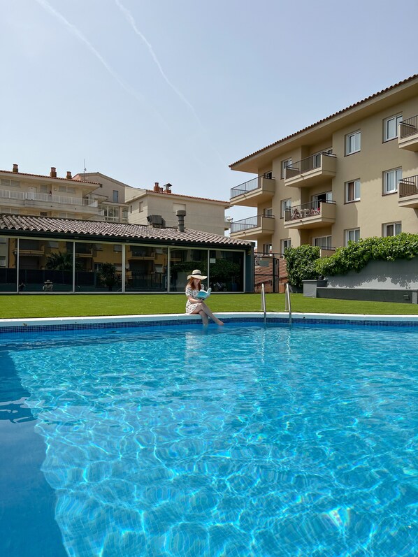 A swimming pool with a person reading a book, surrounded by apartment buildings with balconies.