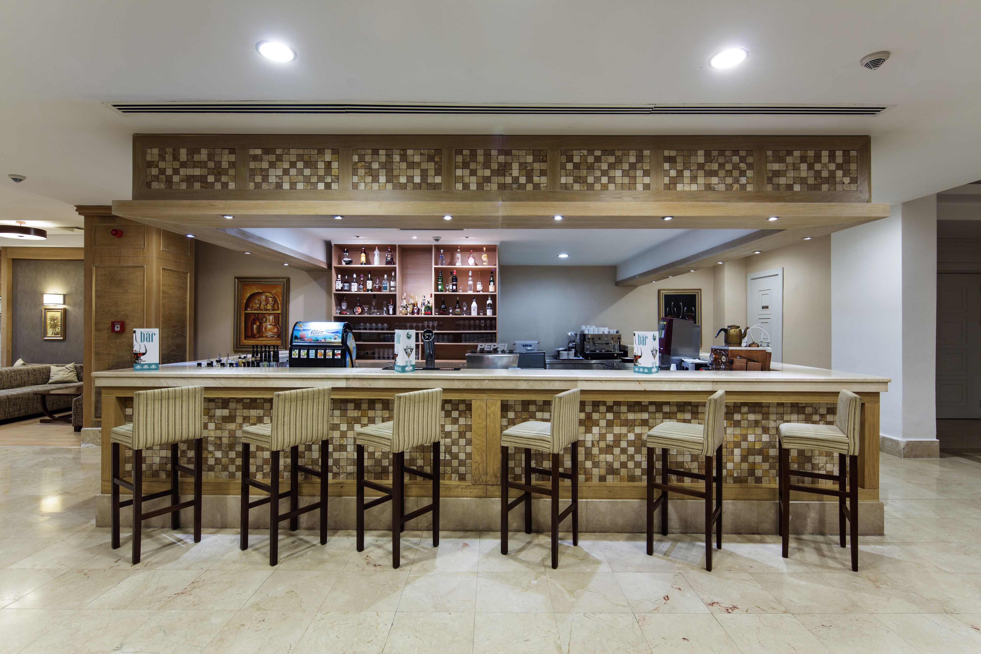 A bar area with a checkered tile backsplash, bar stools, and a variety of liquor bottles.