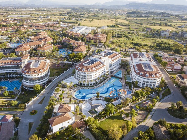 Ett hotellkomplex med flera byggnader, ett centralt poolområde och omgivande grönska.