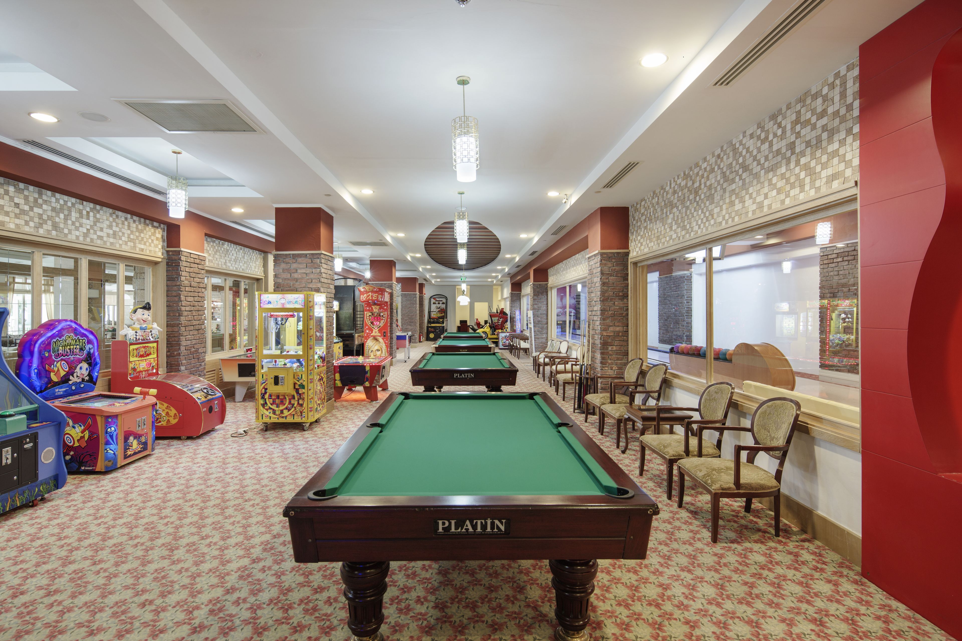 Una sala de billar con mesa de pool verde, sillas y juegos de arcade.