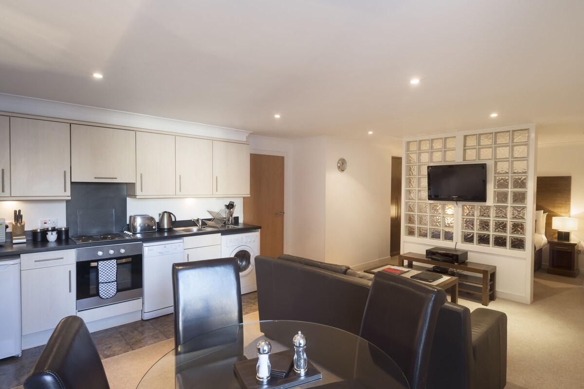 A modern kitchen with white cabinets, a built-in oven, and a dining area with a glass table and black chairs.