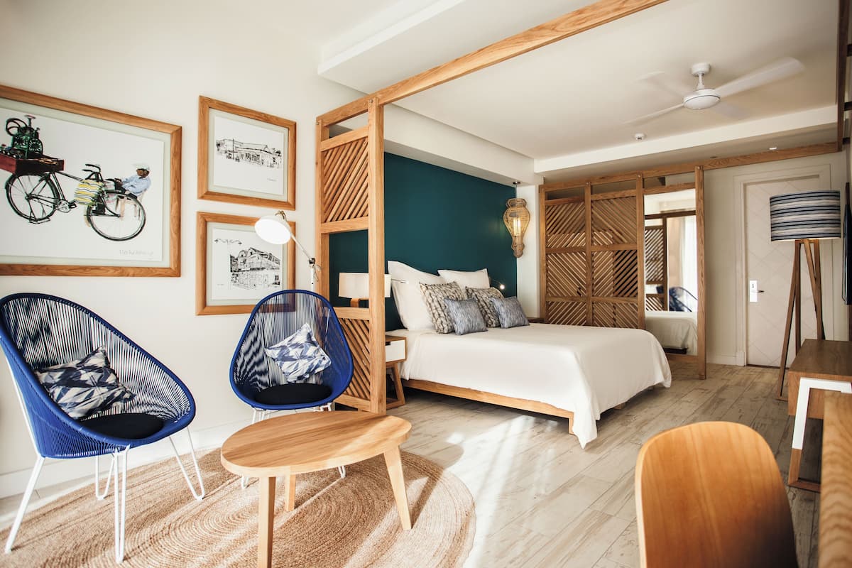 Un dormitorio moderno con una cama, dos sillas azules, una mesa de madera y una lámpara de pie.