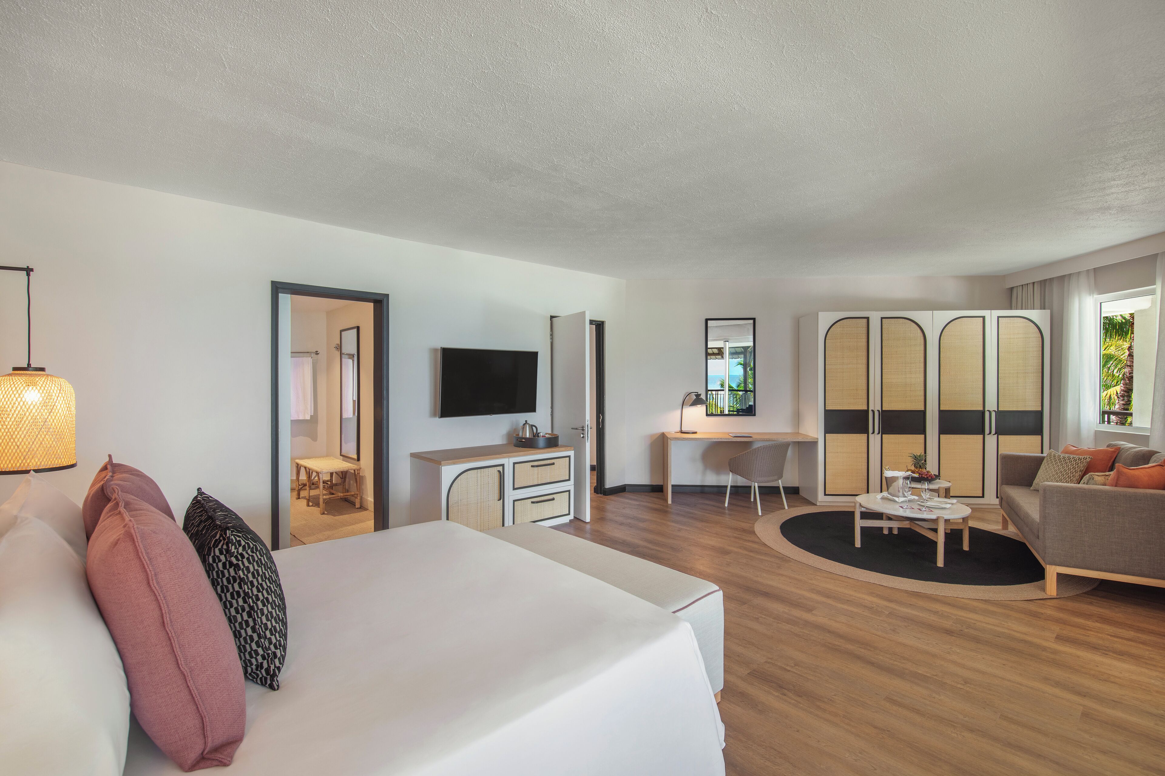 Ein modernes Hotelzimmer mit Bett, Schreibtisch, Fernseher, Sofa und Blick ins Freie.