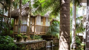 Una località turistica tropicale con cabine a tetto di paglia, una fontana in pietra e vegetazione lussureggiante.