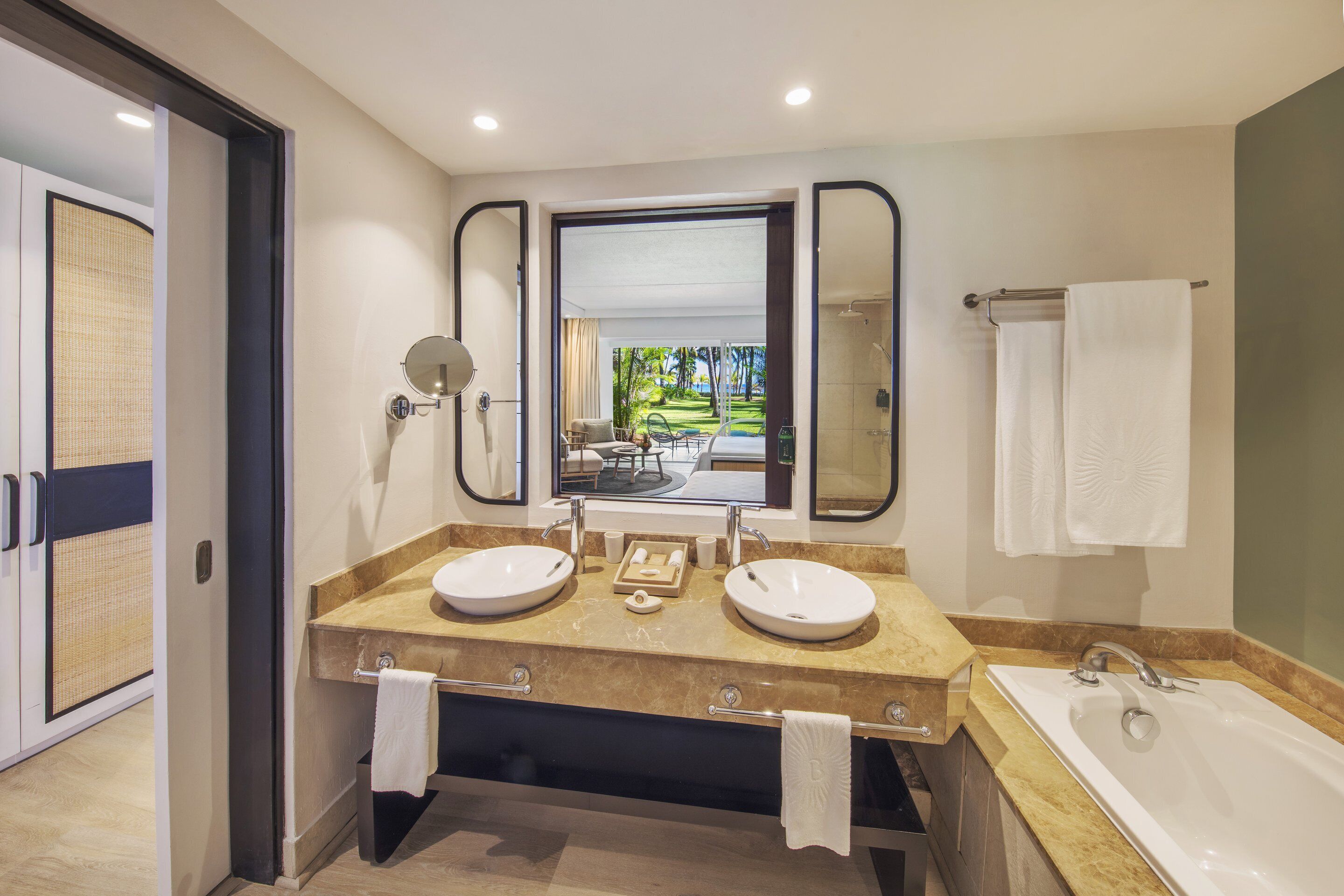 A modern bathroom with two sinks, a large mirror, and a bathtub.