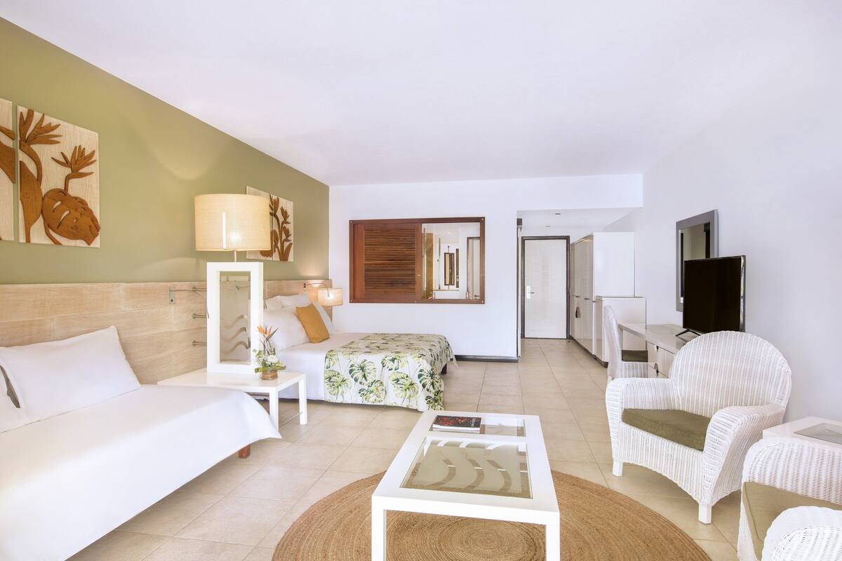 Una habitación de hotel moderna con cama, sofá, mesita de café, televisión y zona de comedor.