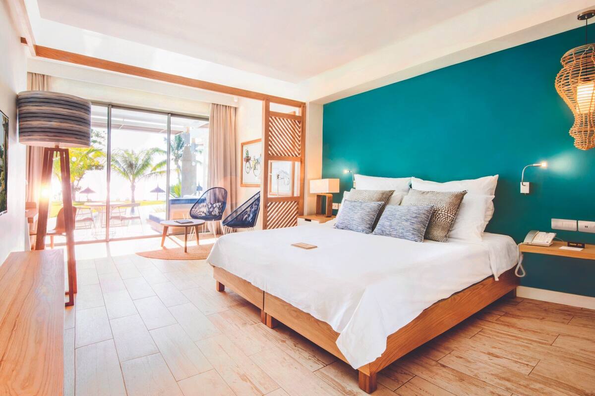 Una habitación de hotel moderna con una cama grande, vistas al exterior y un comedor con mesa y sillas.