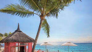 Un ristorante sulla spiaggia con una capanna a tetto di paglia, posti a sedere all'aperto con ombrelloni e vista sull'oceano.