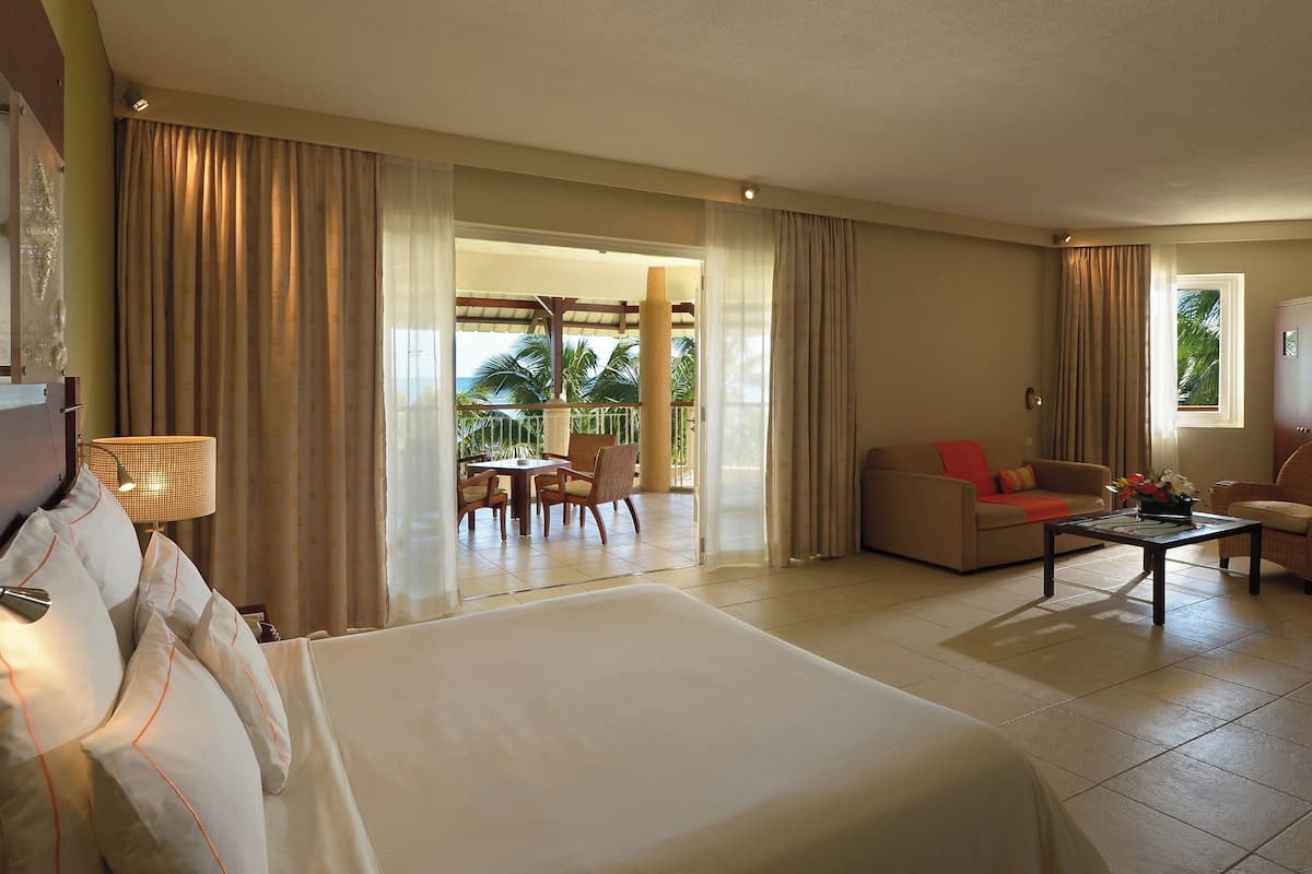 Una habitación de hotel con cama, sofá, mesa de comedor y balcón con sillas.