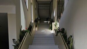 Un escalier moderne avec des marches blanches et des murs de couleur beige, bordé de jardinières ornées de feuillage verdoyant.