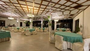 Une salle de banquet avec de nombreuses tables rondes recouvertes de nappes vertes et des chaises blanches.