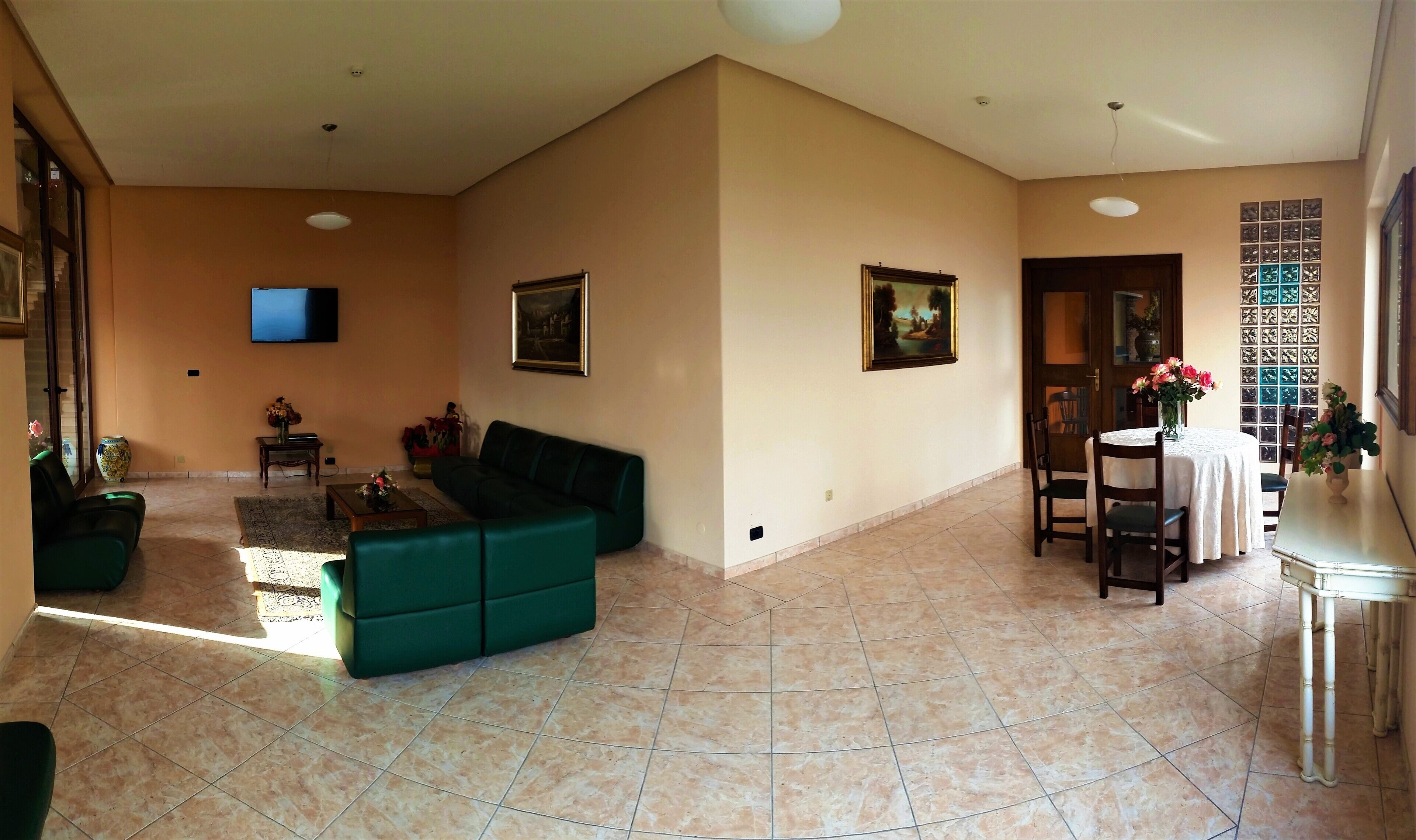 A spacious living room with a green sofa, a flat-screen TV, and a dining area with a table and chairs.