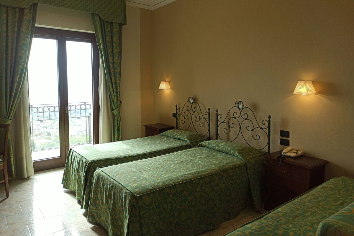 A hotel room with two beds, a balcony, and a view of the city.