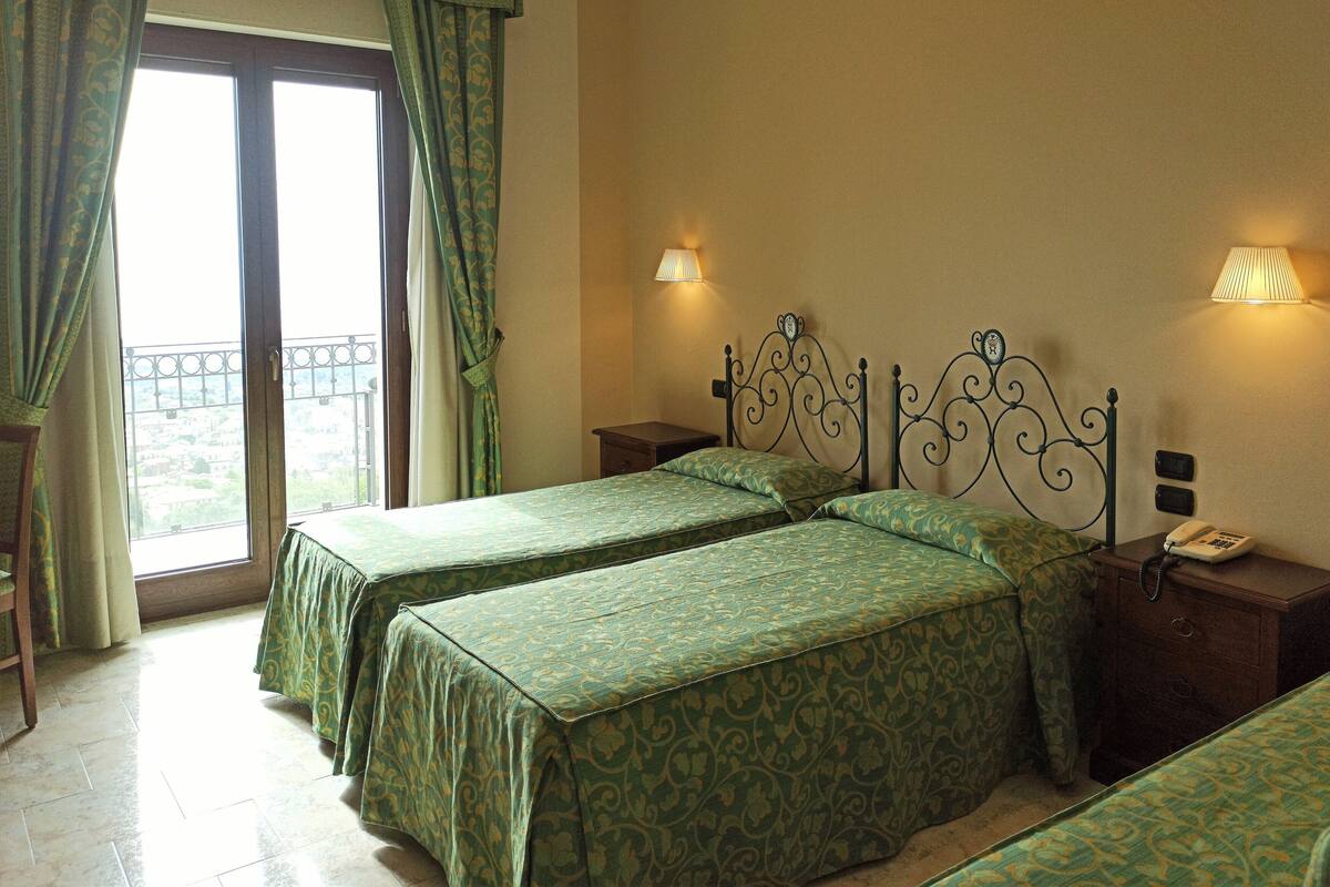A hotel room with two beds, a nightstand with a phone, and a window with curtains.