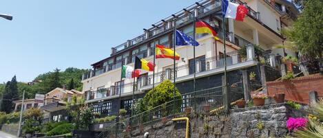 Un hotel con varios balcones, banderas y un muro de piedra con plantas.